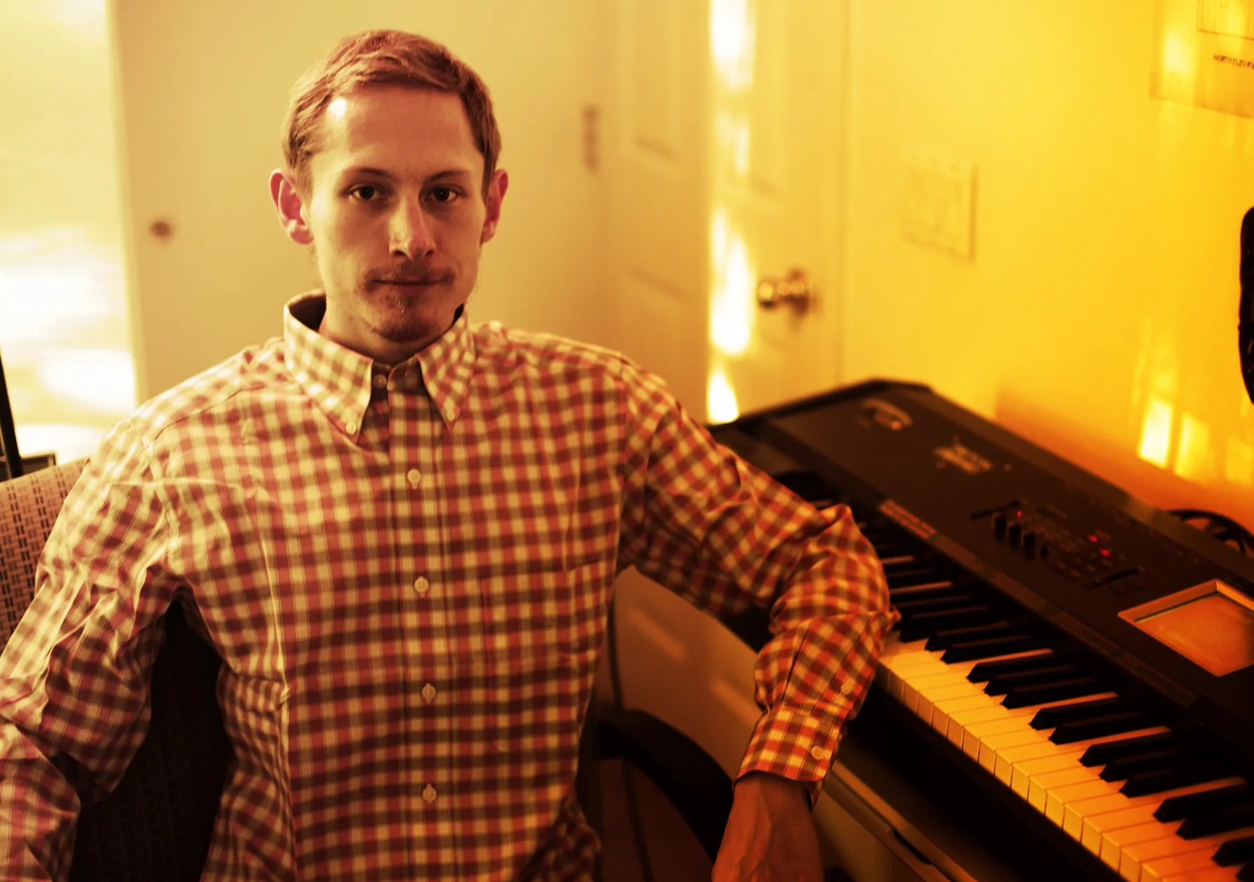 Warm editorial portrait of Ryan seated beside a keyboard